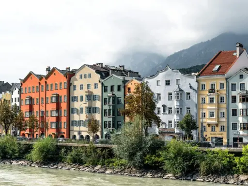 Bunte Häuserzeile am Flussufer, ein Beispiel dafür, was ein Ballungsraum ist: dicht bebaut, mit Bergen im Hintergrund.