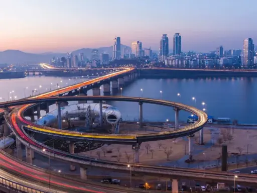 Verkehrsfluss in Seoul bei Nacht, mit Lichtern, die sich auf den Autobahnauffahrten und der Skyline der Stadt spiegeln.