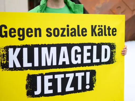 Gelbe Tafel mit schwarzer Schrift: "Gegen soziale Kälte KLIMAGELD JETZT!". Eine Forderung nach sozialer Gerechtigkeit im Klimaschutz.