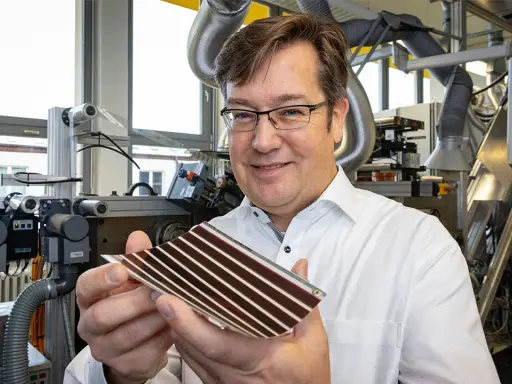 Mann in Labor hält organische PV-Zelle. Die flexible Solarzelle mit Streifen ist ein Produkt fortschrittlicher Forschung.
