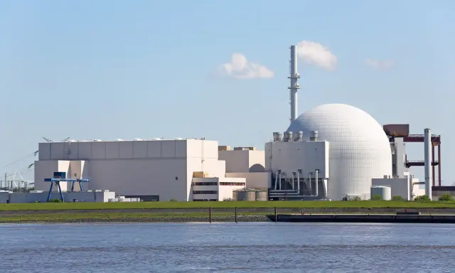 Großes Kernkraftwerk mit Kuppel und Kühlturm am Wasser.