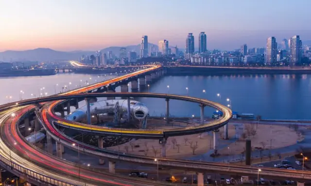 Verkehrsfluss in Seoul bei Nacht, mit Lichtern, die sich auf den Autobahnauffahrten und der Skyline der Stadt spiegeln.