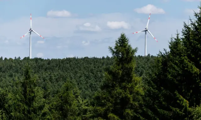 Zwei Windräder ragen über einen dichten Wald. Ein Onshore-Windpark in Deutschland, der saubere Energie erzeugt.
