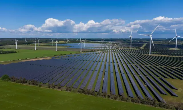 Großes Feld mit Windkraftanlagen und Photovoltaik-Modulen unter blauem Himmel mit Wolken.