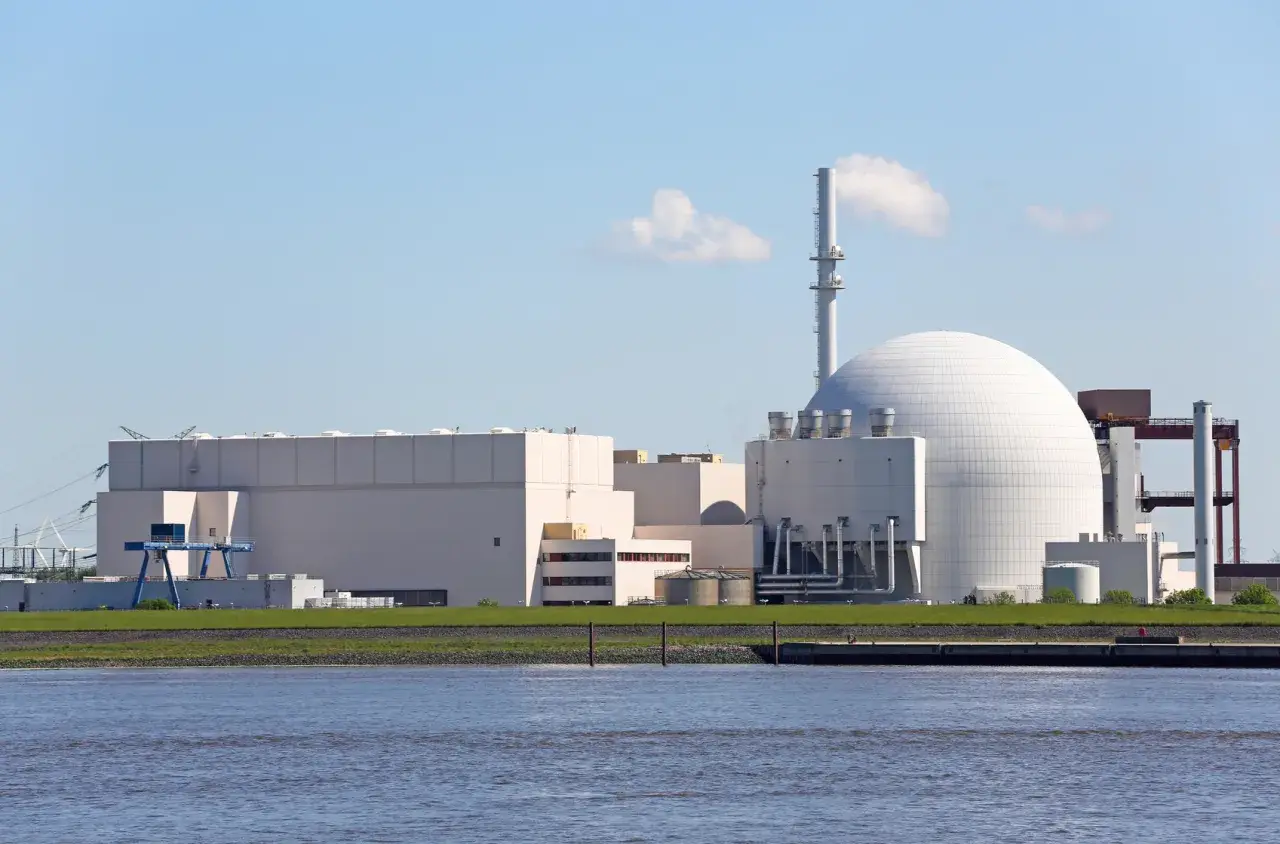 Großes Kernkraftwerk mit Kuppel und Kühlturm am Wasser.
