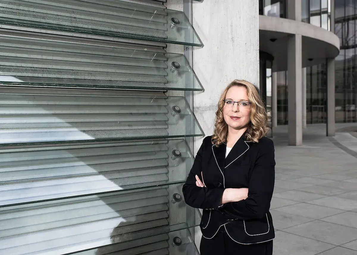 Frau Kemfert steht selbstbewusst vor einer modernen Glasfassade.