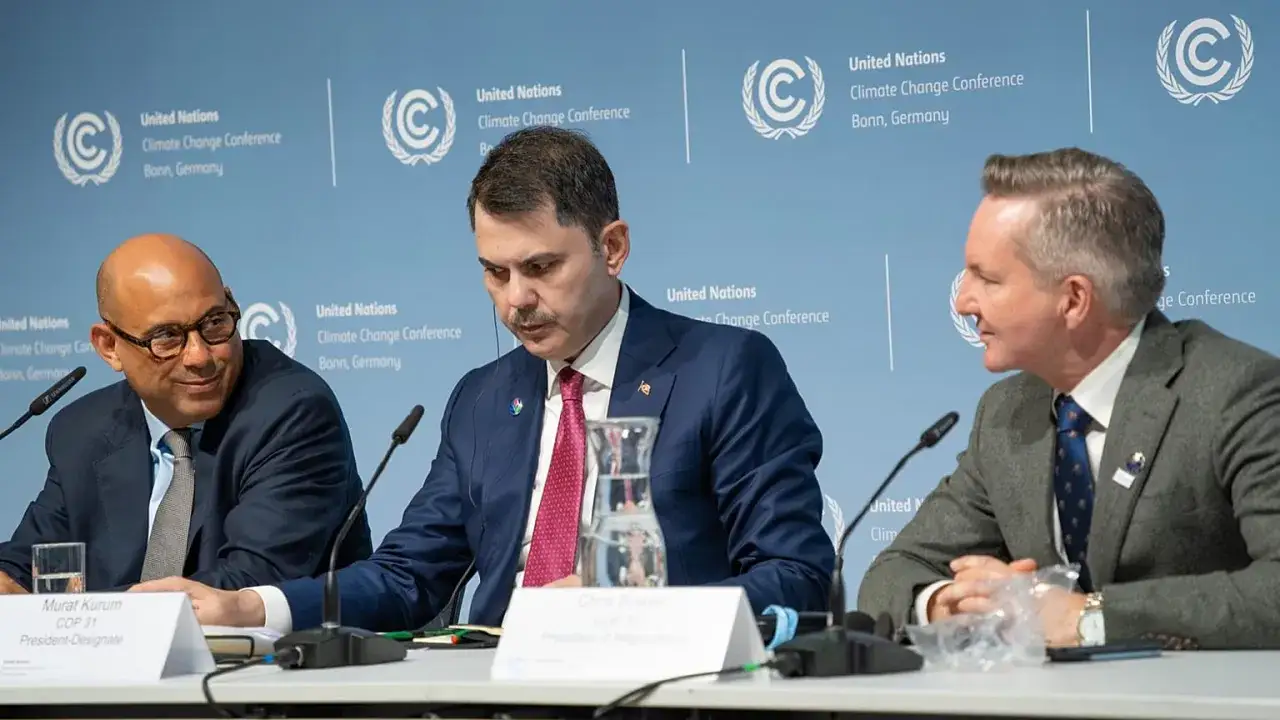 Drei Teilnehmer der Klimakonferenz in Bonn diskutieren. Ein Mann mit Brille lächelt, während ein anderer nachdenklich blickt.