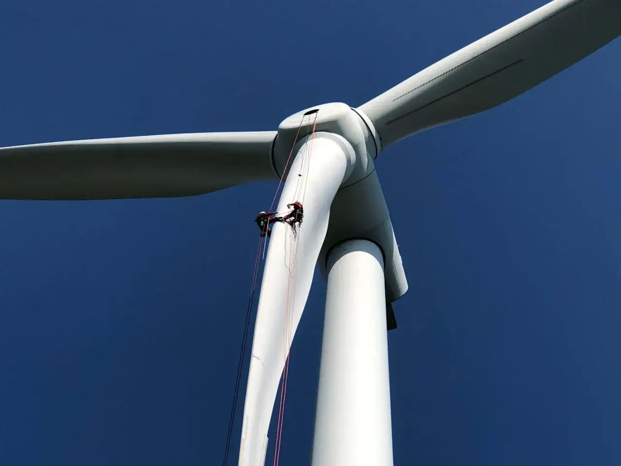 Zwei Techniker seilen sich an einer Windkraftanlage ab, um Wartungsarbeiten während der Laufzeit durchzuführen.