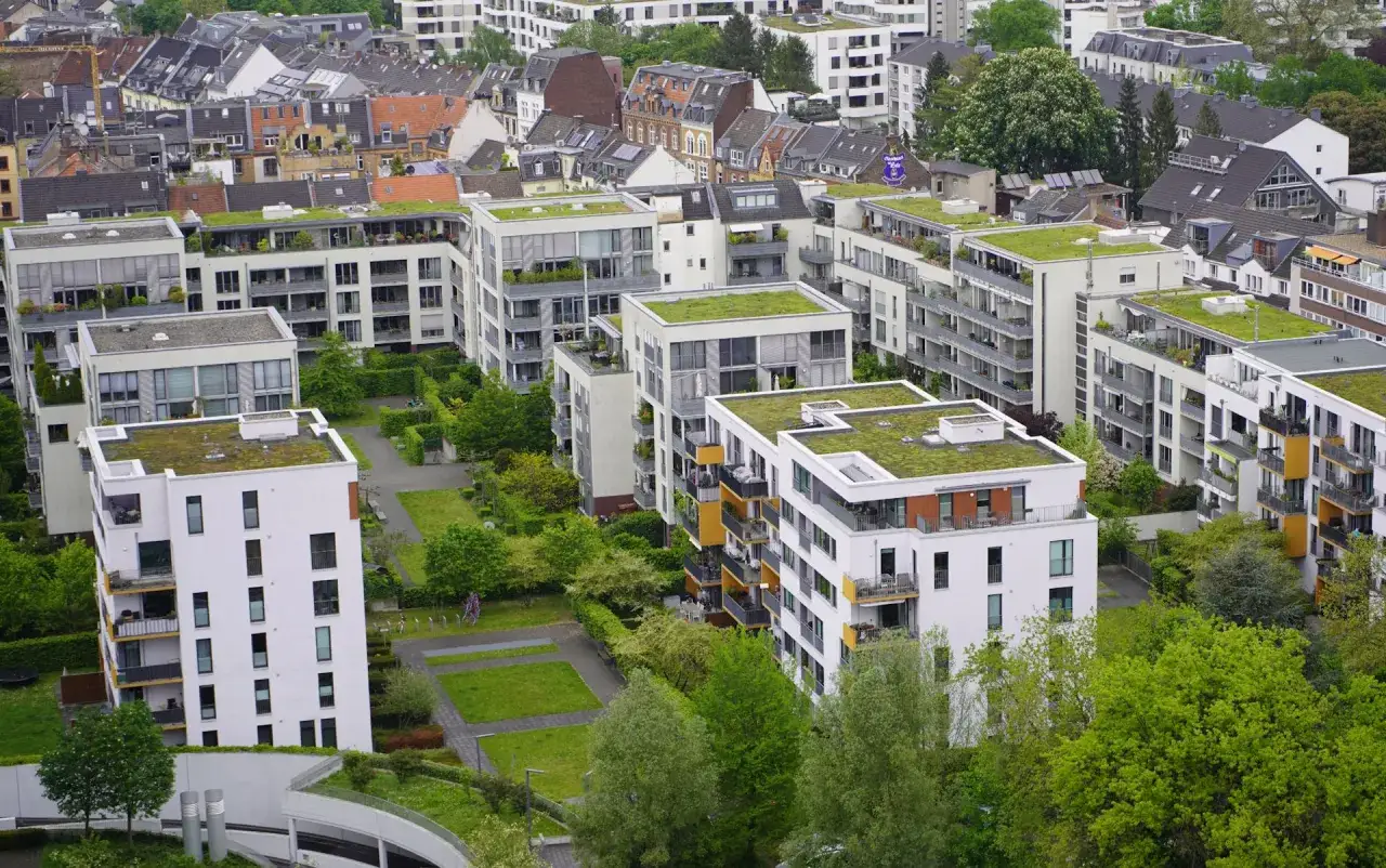 Moderne Wohngebäude mit begrünten Dächern und Balkonen prägen das Bild einer offenen Stadt. Grünflächen und Bäume durchziehen die Architektur.