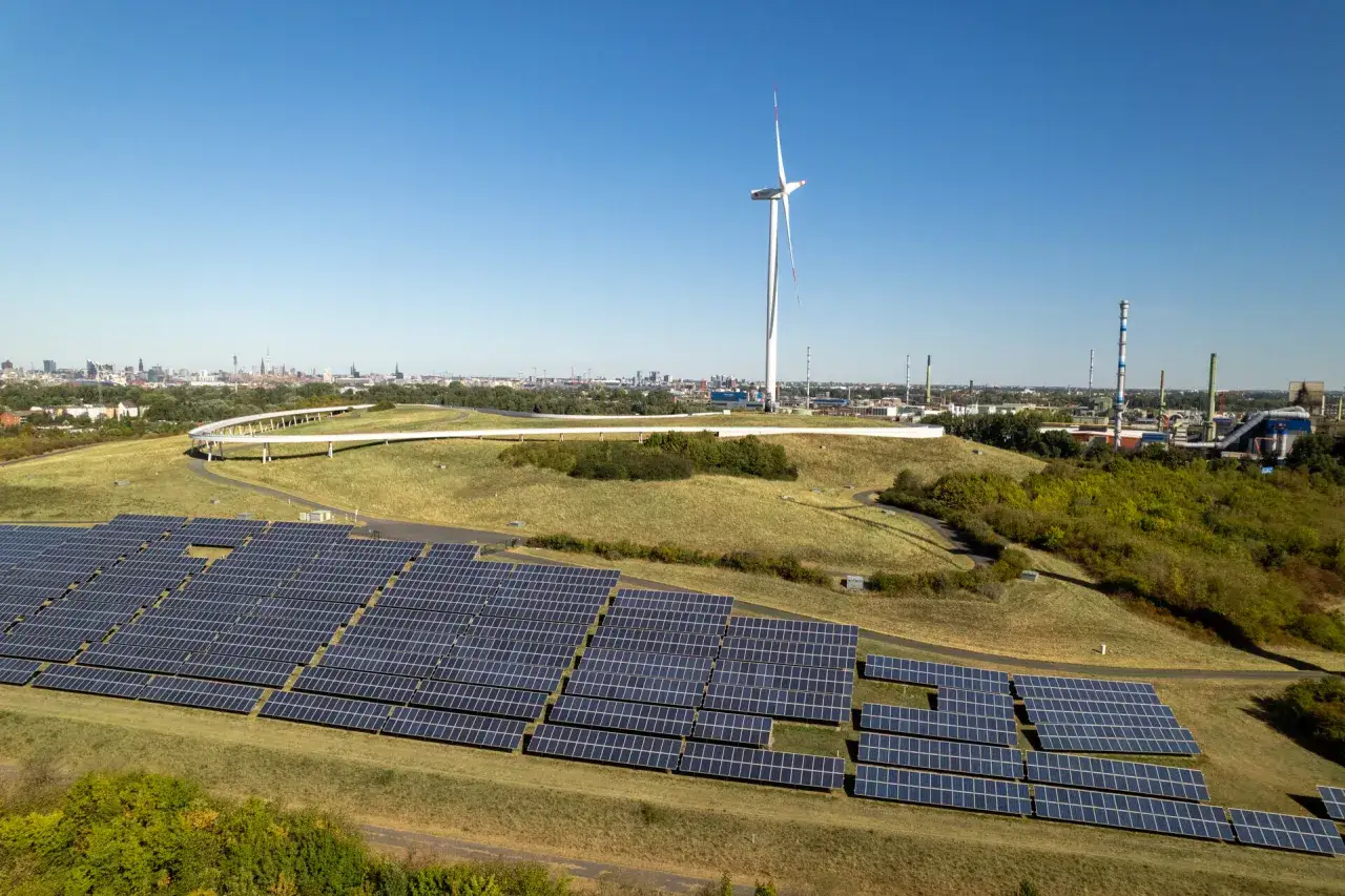 Große Solaranlage und Windrad im Vordergrund, im Hintergrund die Skyline von Hamburg. Ein Zeichen für erneuerbare Energien in Hamburg.