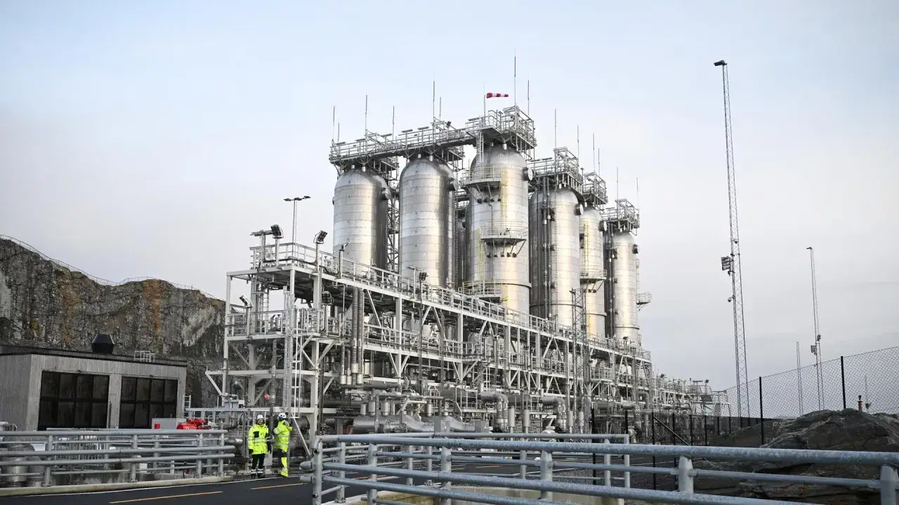 Industrielle Anlage mit großen Tanks und Rohrleitungen, Teil einer carbon management strategie. Zwei Personen in Warnwesten inspizieren das Gelände.
