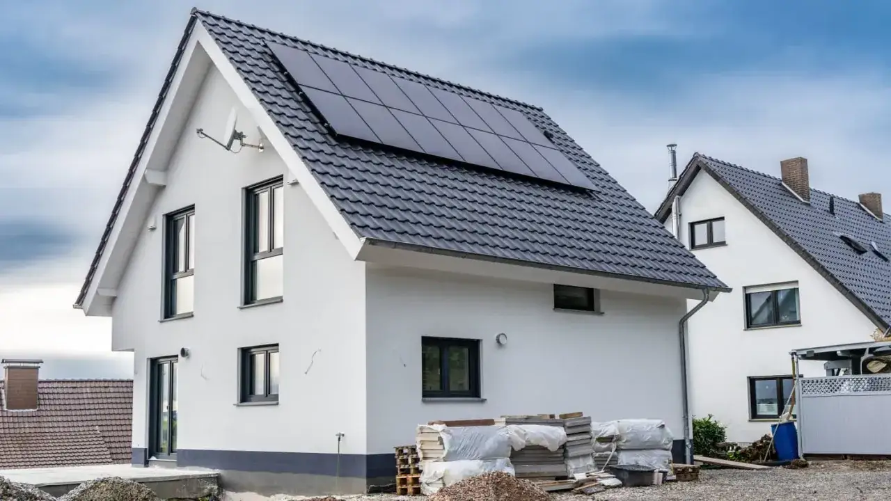 Neubau mit Solaranlage auf dem Dach, die die Sonne als Energiequelle nutzt. Materialstapel deuten auf weitere Bauarbeiten hin.