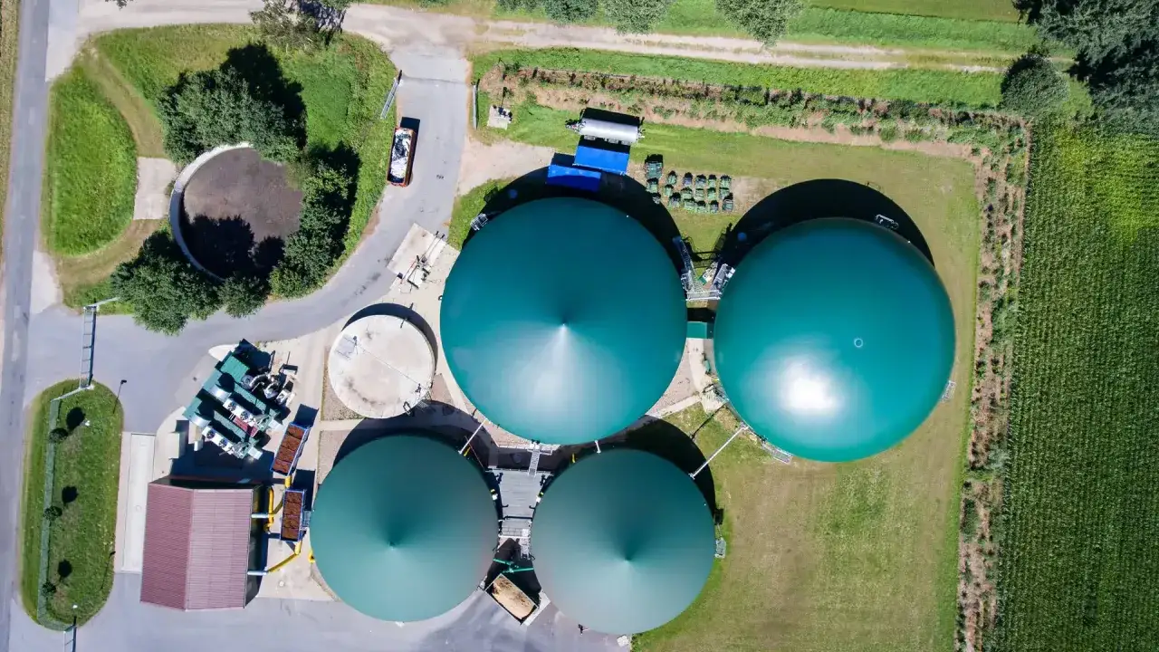 Luftaufnahme einer Biogasanlage mit großen grünen Gasbehältern. Ein LKW ist zu sehen, der Material für das biogas transportieren könnte.