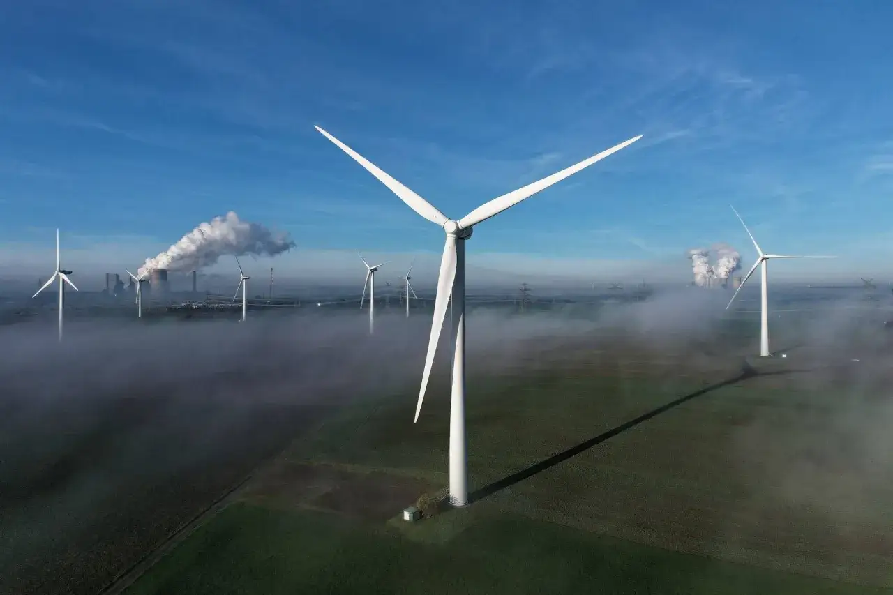 Eine kleinwindkraftanlage NRW steht im Vordergrund, während im Hintergrund ein Kraftwerk mit Dampfschwaden und weitere Windräder im Nebel zu sehen sind.