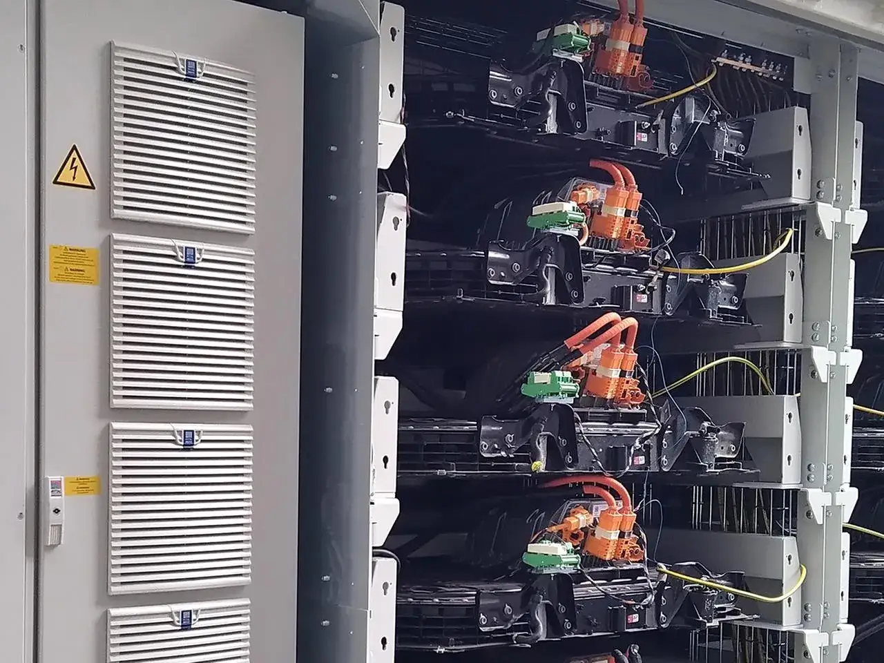 Ein Rack mit mehreren Modulen, die für Second-Life-Batterien vorbereitet sind. Orange und grüne Kabel verbinden die einzelnen Einheiten.