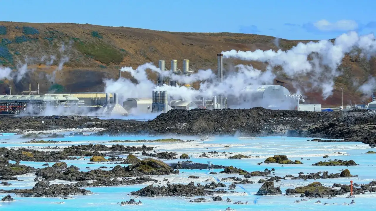 Geothermieanlage auf Island mit dampfenden Schornsteinen &uuml;ber blauem Wasser. Die Strompreise auf Island sind hier durch nachhaltige Energie beeinflusst.