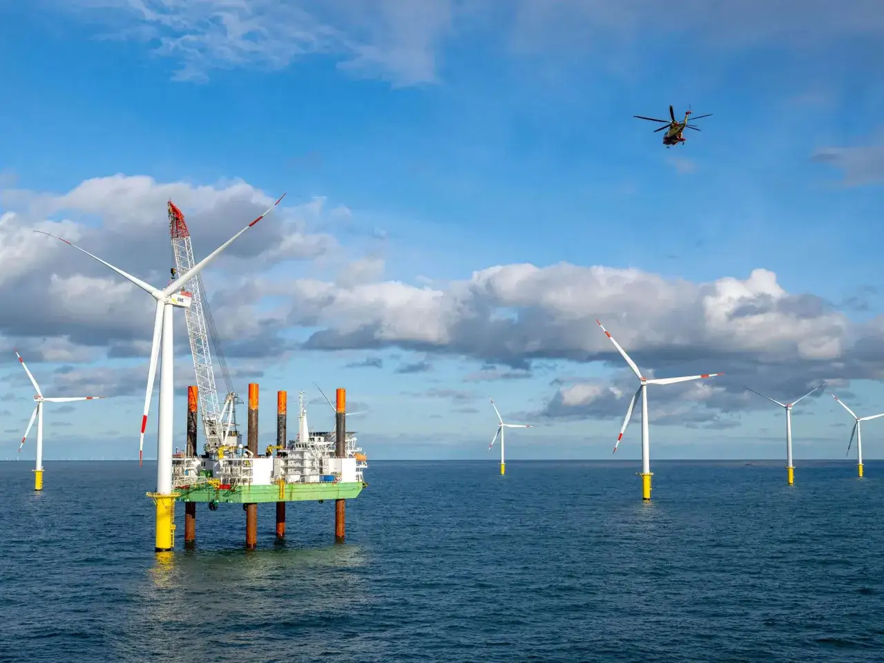 Windkraftanlagen und ein Bohrinsel-ähnliches Schiff im Meer vor Borkum. Ein Hubschrauber fliegt über die Szenerie, die an die Gasförderung Borkum erinnert.
