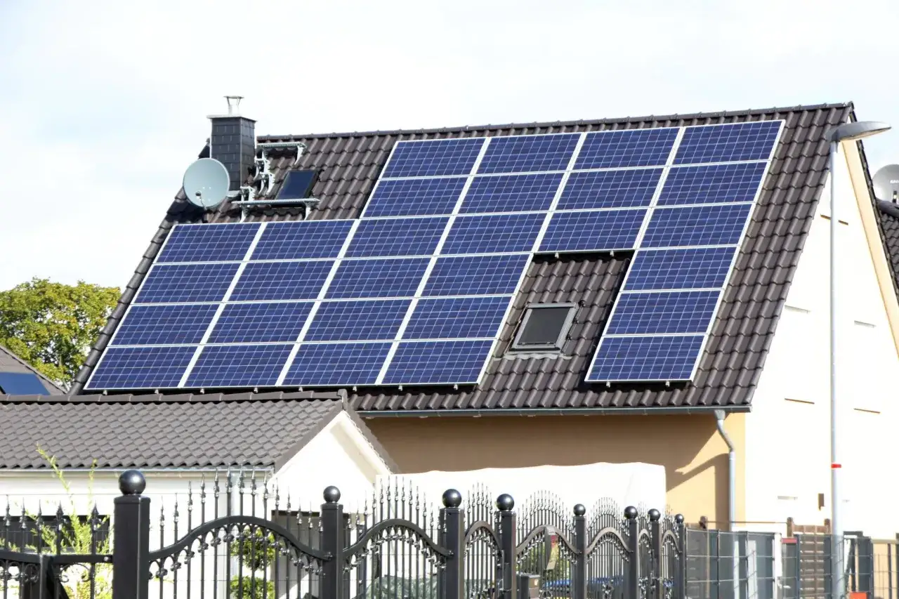 Ein Hausdach mit vielen Solarmodulen, die erneuerbare Energie von der Sonne einfangen. Ein Schornstein und eine Satellitenschüssel sind ebenfalls sichtbar.