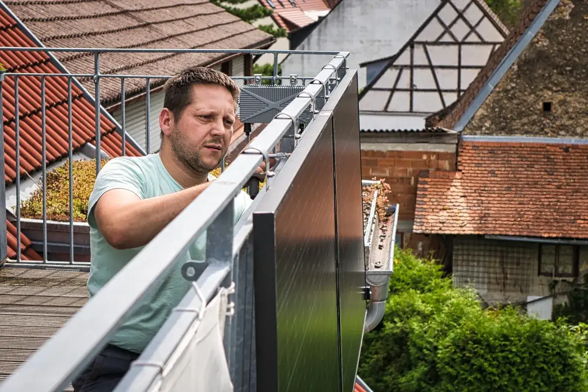 Mann montiert Balkonkraftwerk in Niedersachsen. Solarmodule werden an einem Geländer befestigt, im Hintergrund Fachwerkhäuser.