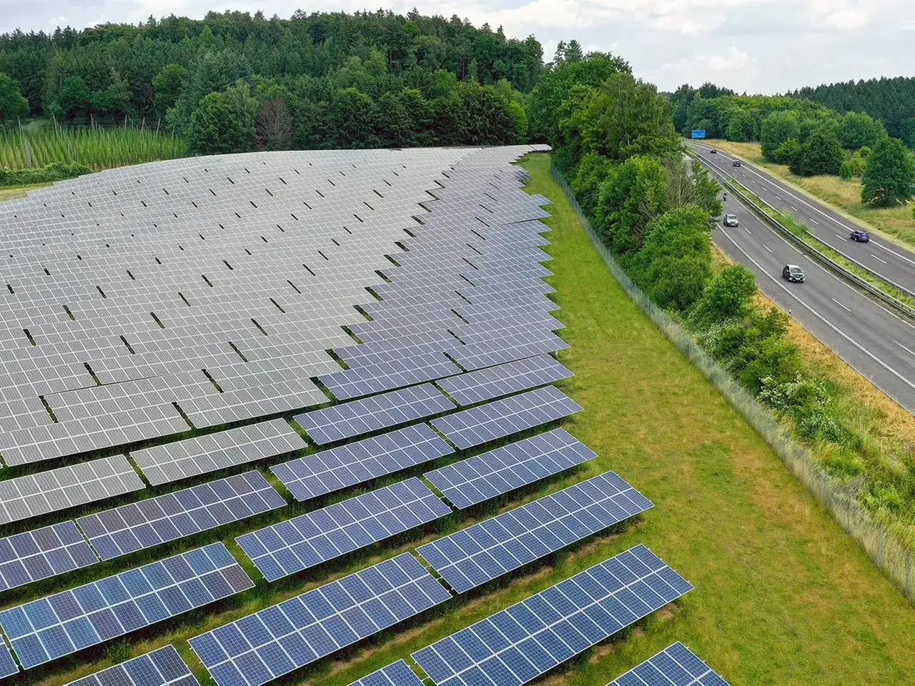 Große Solaranlage in Deutschland, die den aktuellen Stand der erneuerbaren Energien zeigt. Autos fahren auf der Autobahn daneben.