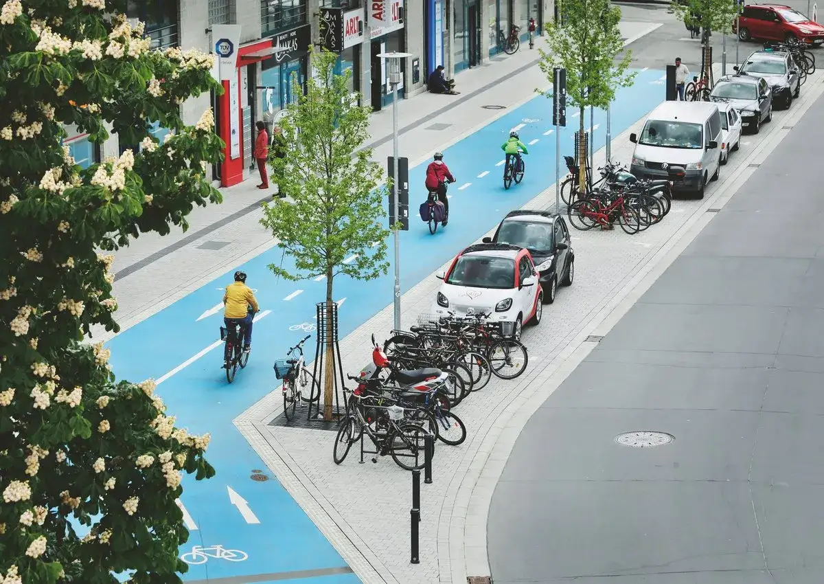 Fahrradfahrer auf blauem Radweg, Autos und Bäume symbolisieren nachhaltige Quartiersentwicklung in einer modernen Stadt.