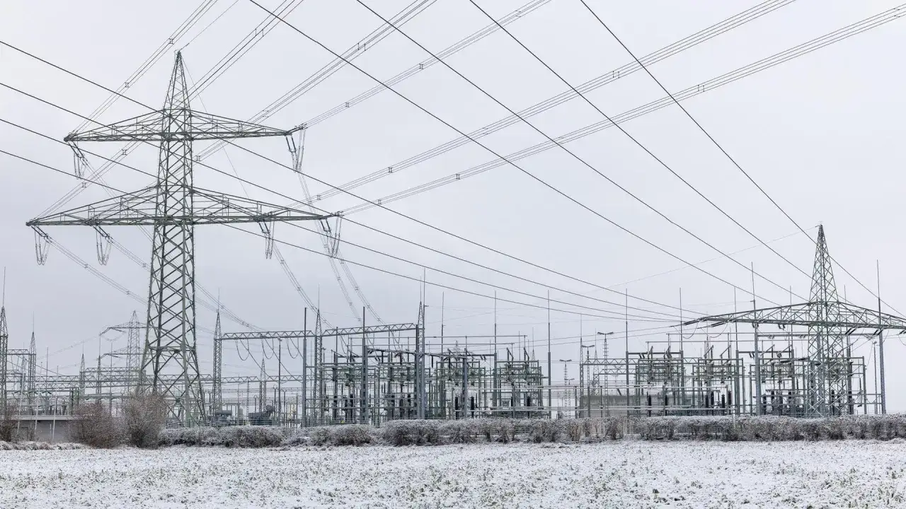 Ein Umspannwerk mit hohen Strommasten und Leitungen, die zeigen, was ist Hochspannung. Im Vordergrund liegt Schnee.