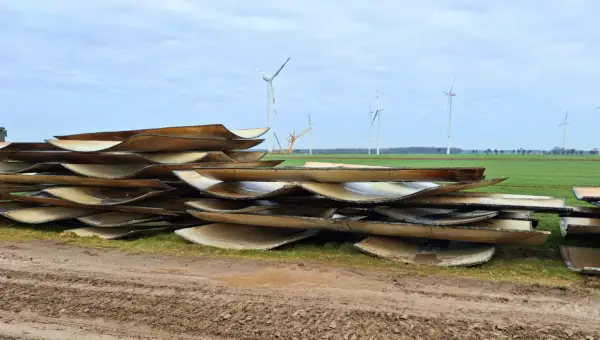 Stapel von Rotorblättern von Windkraftanlagen, bereit für das Recycling. Im Hintergrund sind weitere Windräder zu sehen.
