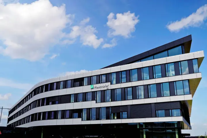 Modernes Gebäude des Fraunhofer IEE mit geschwungener Fassade und vielen Fenstern unter blauem Himmel mit Wolken.