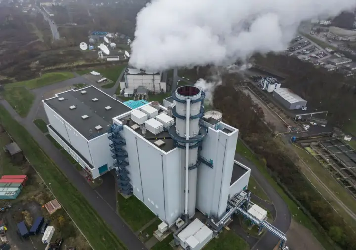 Dampf steigt aus einem modernen Gaskraftwerk in Deutschland auf. Satellitenschüsseln und ein Parkplatz sind in der Nähe zu sehen.